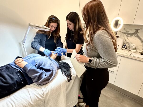 Students practicing dermaplaning on a classmate in a MedBeautyLA treatment room while the instructor looks on